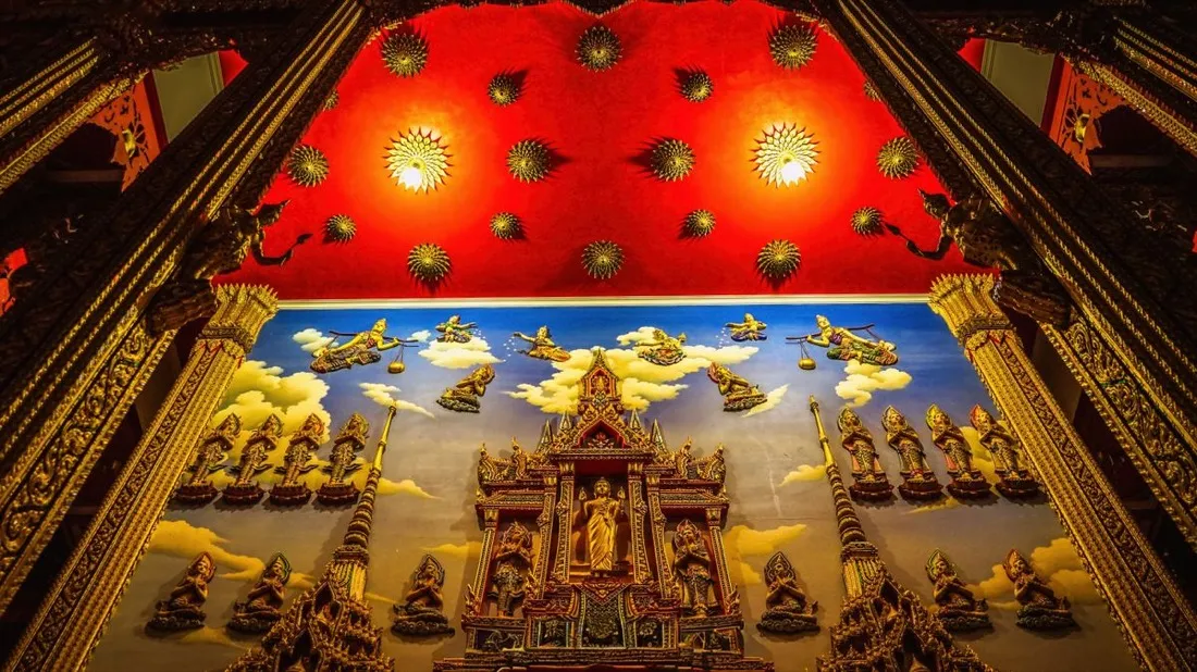 An ornate temple ceiling with a red upper wall, gold medallions and a painted cloud mural