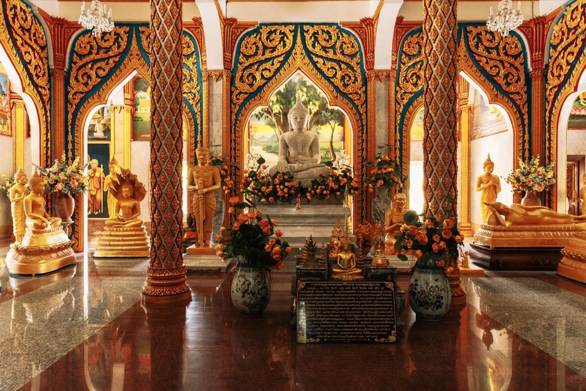 An ornate temple hall with many golden Buddha statues and orange flower offerings
