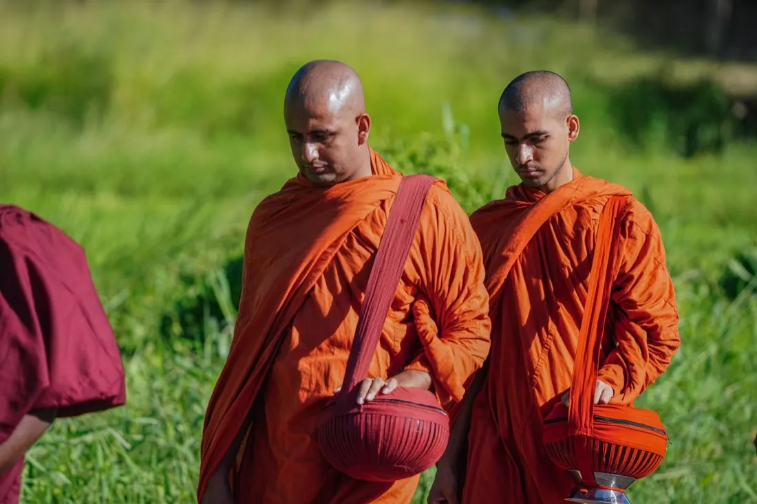 Two Buddhist monks in orange robes walking with alms bowls
